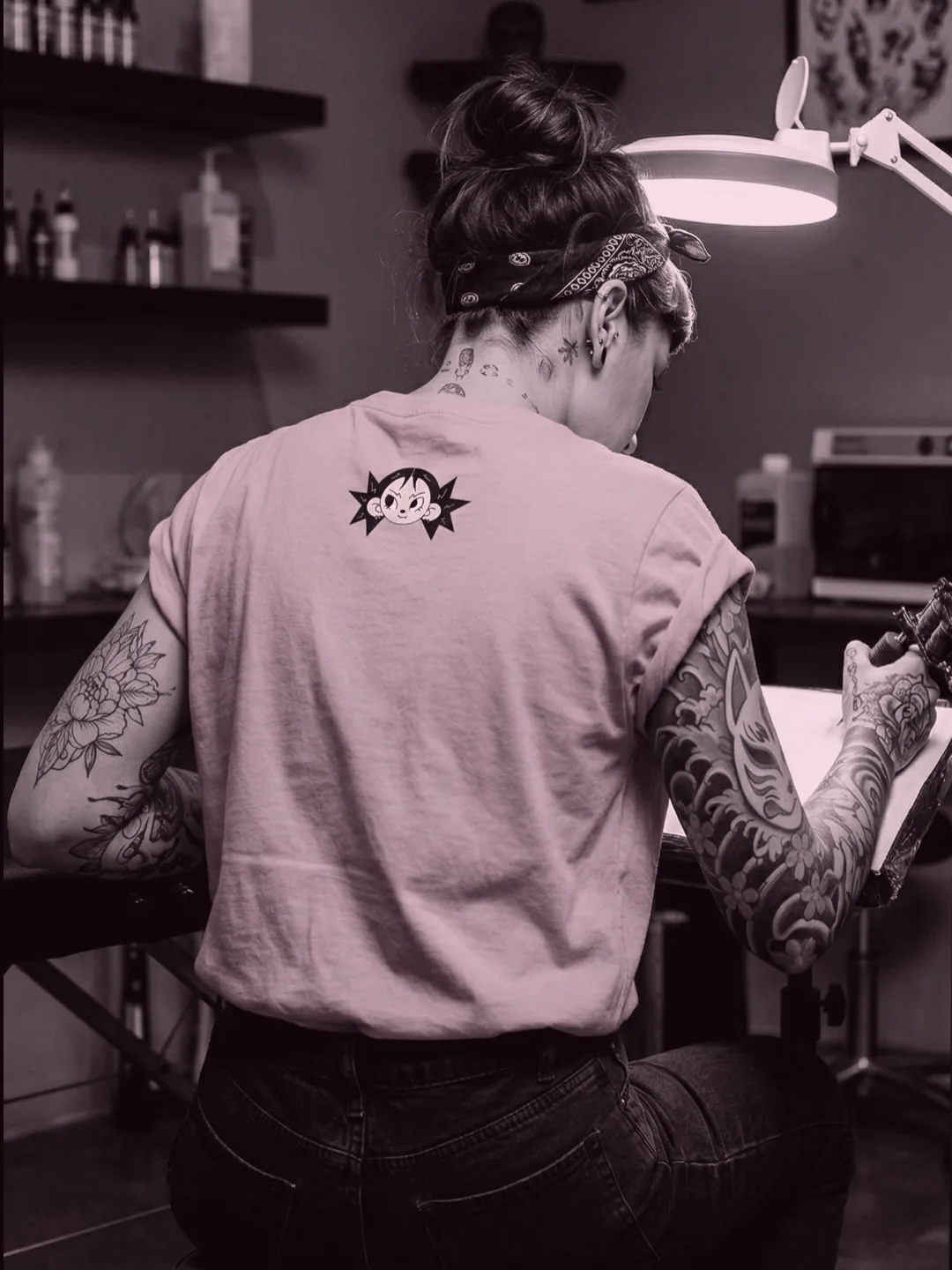 Moxie de dos, penchée sur une planche à dessin dans son salon de tatouage.